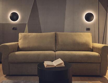 Helles Sofa vor einer geometrisch gestalteten Wand mit zwei runden Wandleuchten im Hotel Villa Alberta.