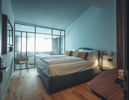 Suite Aura con letto matrimoniale, pavimento in legno, illuminazione calda, vasca da bagno freestanding e finestre.