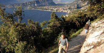 Hiker on a rocky hiking trail above Lake Garda, overlooking the lake and the surrounding landscape.