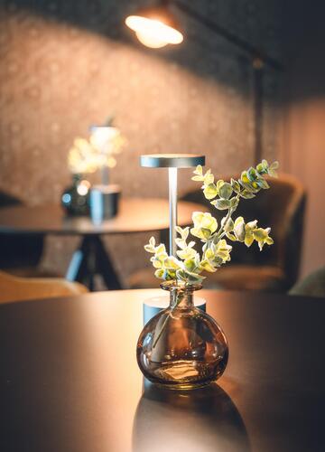 Piccolo vaso di vetro con fiori bianchi su un tavolo scuro in un ambiente accogliente e illuminato da una luce calda.
