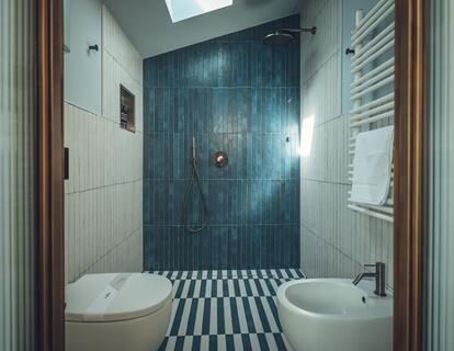Bagno della Suite Aura con piastrelle bianche e blu, WC, bidet e doccia a filo pavimento.