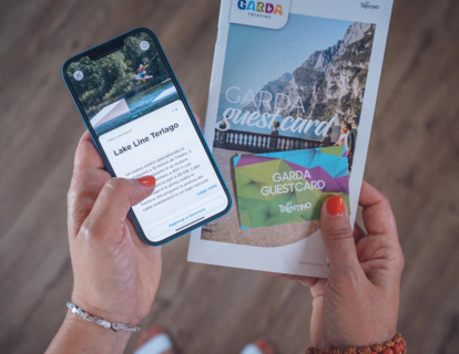 Person holding a smartphone and a Garda Guest Card tourist information brochure.