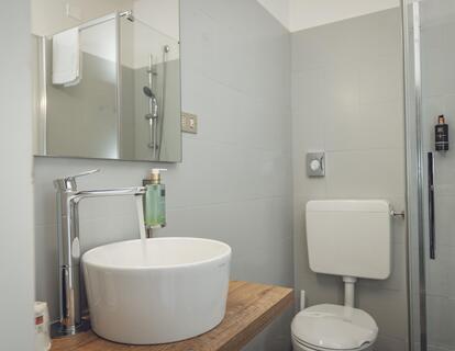 Badezimmer mit Waschbecken, großem Wandspiegel, WC und Dusche im Hotel Villa Alberta.