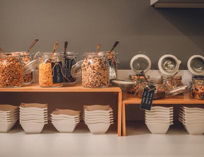 Breakfast buffet at Hotel Villa Alberta with various types of muesli, cereals and white bowls.