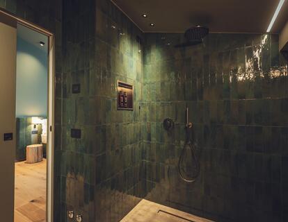 Shower in Suite Dryas with dark green tiles, a niche for toiletries, a handheld showerhead and a rainfall showerhead.