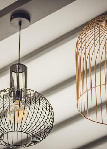 Dekorative Hängeleuchten aus Metallgeflecht in verschiedenen Formen und Größen an einer hellen Decke.