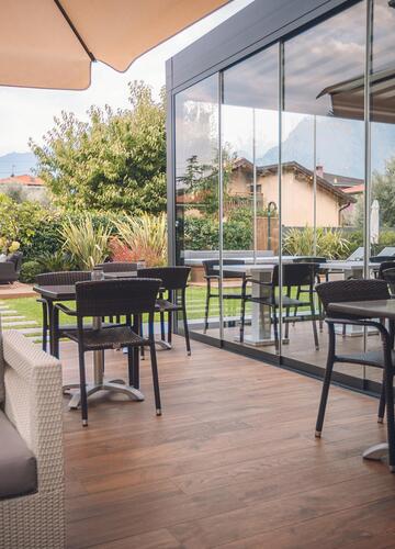 Terrazza dell'hotel con divani imbottiti, tavoli, sedie e ombrelloni davanti a un'ampia vetrata.