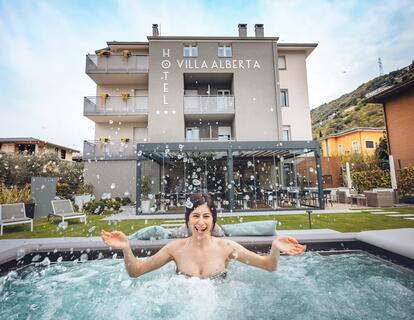 Donna nella vasca idromassaggio nel giardino dell'Hotel Villa Alberta a Torbole, con vista sull'edificio dell'hotel.