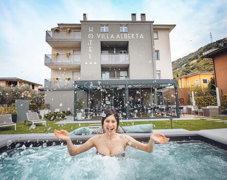 Frau im Whirlpool im Garten des Hotels Villa Alberta in Torbole mit Blick auf das Hotelgebäude.
