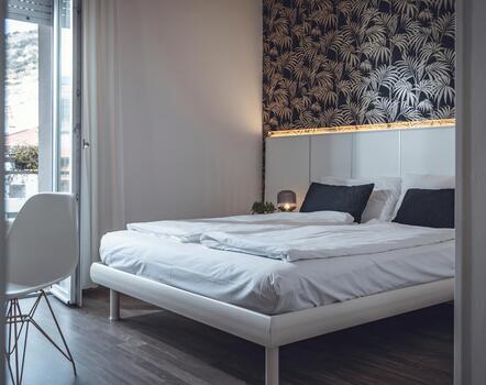 Modernes Hotelzimmer mit Doppelbett, weißer Bettwäsche, gemusterter Wandtapete und Balkon.