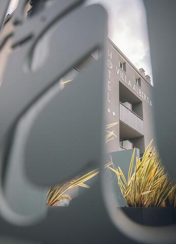 Primo piano del logo e della scritta dell'Hotel Villa Alberta con l'edificio dell'hotel sullo sfondo.