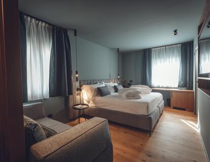 Modern hotel room with a double bed, grey sofa and wooden flooring at Hotel Villa Alberta.