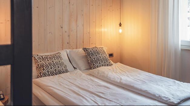 Hotelzimmer mit Doppelbett, Nachttisch, warmem Licht und großem Fenster.