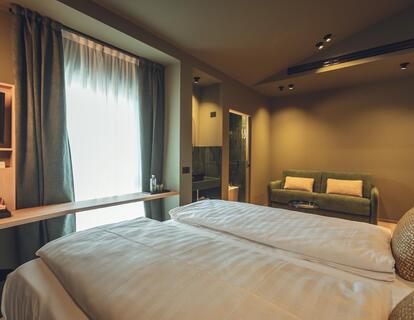 Suite Dryas with a double bed, window, television, sofa, freestanding washbasin and a view of the bathroom.