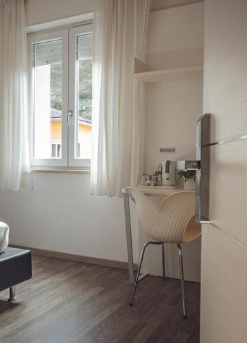 Helles Hotelzimmer mit Doppelbett, Fernseher, Schreibtisch, Fenster und geöffneter Zimmertür.
