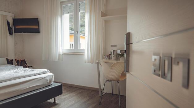 Helles Hotelzimmer mit Doppelbett, Fernseher, Schreibtisch, Fenster und geöffneter Zimmertür.