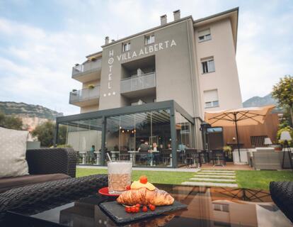 Croissant, frutta e bevanda su un tavolo in terrazza con vista sul giardino e sull'Hotel Villa Alberta a Torbole.