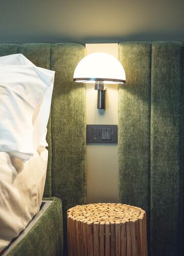 Close-up of Suite Dryas with a double bed, a green upholstered headboard and an illuminated bedside lamp.