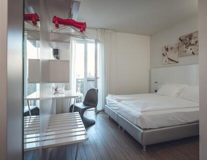 Helles Hotelzimmer mit Doppelbett, weißer Bettwäsche, Schreibtisch und Holzboden im Hotel Villa Alberta.