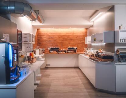 Hotel breakfast buffet with stainless steel appliances, white cabinets and an orange-lit back wall.