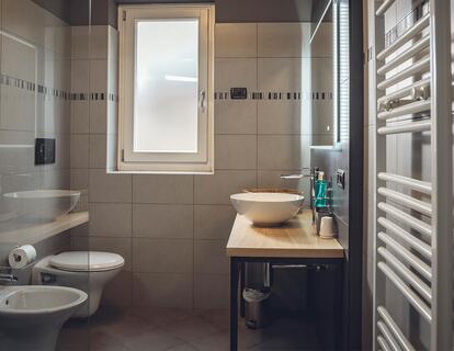 Modernes Badezimmer mit Waschbecken auf einer Holzablage, WC, Bidet und Fenster im Hotel Villa Alberta.