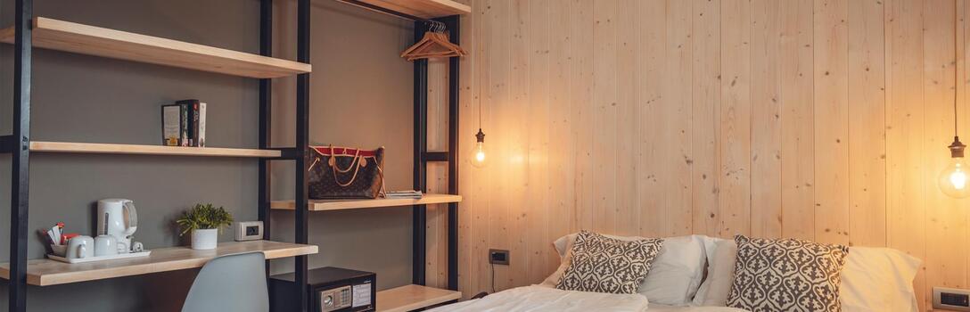 Modernes Hotelzimmer mit Doppelbett, offenem Regal, Schreibtisch und warm beleuchteter Holzwand.