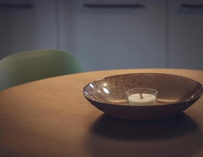 Detailaufnahme einer dekorativen Schale auf einem runden Holztisch mit grünem Polsterstuhl im Hotel Villa Alberta.