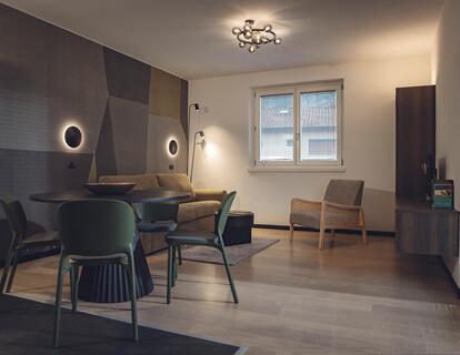 Moderne Wohnbereich mit einem Tisch, Stühlen, Sofa, Sessel und Wandleuchten im Hotel Villa Alberta.