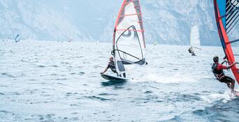 Several windsurfers with colourful sails on Lake Garda, with the surrounding mountain landscape in the background.