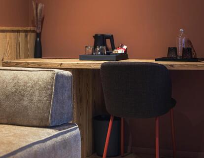 Gemütliche Sitzecke im Hotelzimmer mit gepolstertem Sofa, Schreibtisch aus Holz, Stuhl, Holzboden und warmer Beleuchtung.