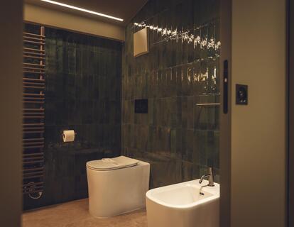 View into the bathroom of Suite Dryas with dark green tiles, a toilet and bidet.