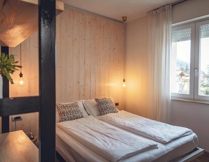 Helles Hotelzimmer mit Doppelbett, Holzwand, warmen Wandleuchten und Fenster.
