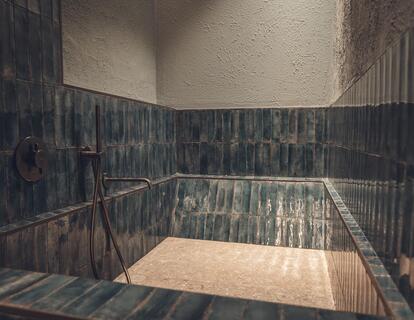Modern shower area with dark blue tiles, rainfall shower and stone flooring at Hotel Villa Alberta.