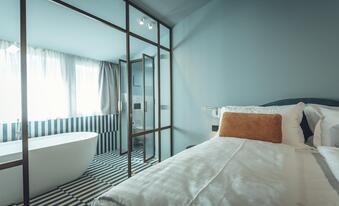 Suite Aura mit Doppelbett, hellblauen Wänden, schwarz-weiß gemustertem Fliesenboden und Blick auf die freistehende Badewanne hinter einer Glaswand.
