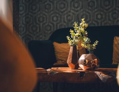 Piccolo tavolo con vaso di fiori tra poltrone imbottite davanti a una parete decorata.
