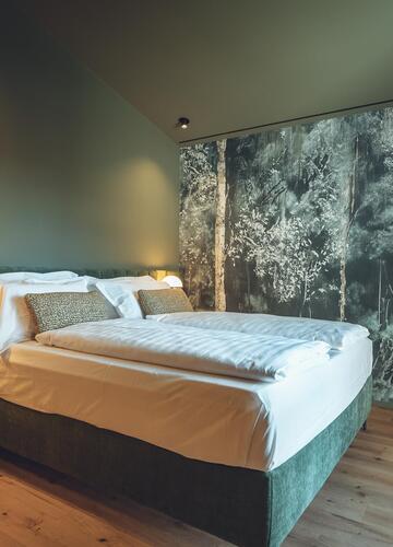 Suite Dryas mit Doppelbett, Holzboden, grüner Wand und floraler Wandtapete.