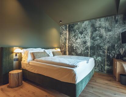 Suite Dryas con letto matrimoniale, pavimento in legno, parete verde e carta da parati floreale.