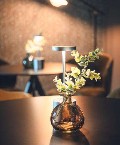 Dettaglio di una piccola composizione di fiori bianchi in un vaso di vetro su un tavolo scuro, nell’ambiente interno elegantemente illuminato dell’Hotel Villa Alberta.