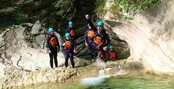 Group of people canyoning with helmets and protective gear in a rocky gorge with turquoise water.