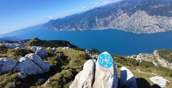 Punto panoramico roccioso con un segnavia e vista panoramica sul Lago di Garda e sulle montagne circostanti.
