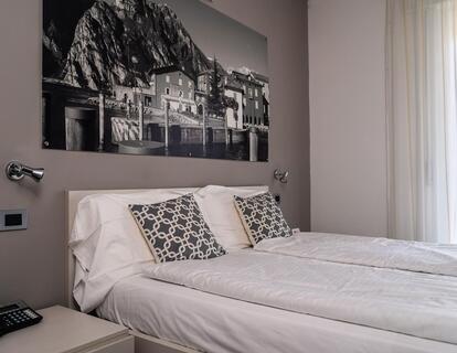 Helles Hotelzimmer mit Doppelbett, gemusterten Kissen, Nachttisch und großem Schwarz-Weiß-Bild über dem Bett.