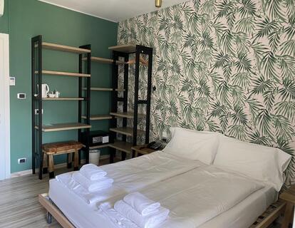 Modernes Hotelzimmer mit Doppelbett, grüner Wand, gemusterter Tapete und offenem Kleiderschrank.